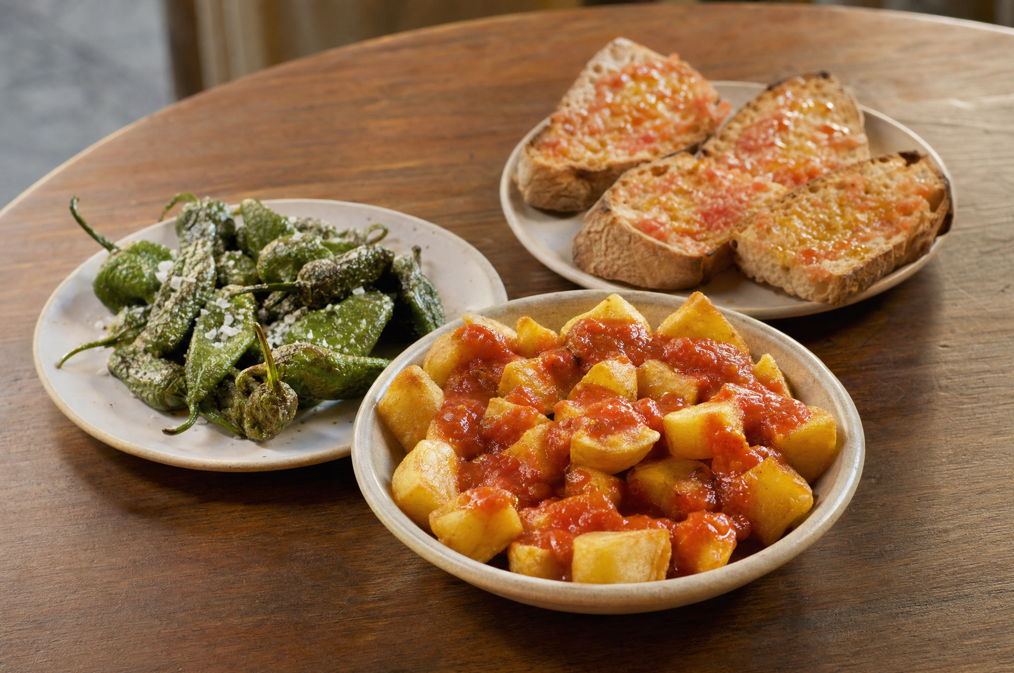 Tapas españolas vegetarianas: patatas bravas, pan con tomate y pimientos de Padrón.